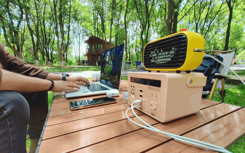 Portable methanol power unit running a laptop and fan at a campsite table
